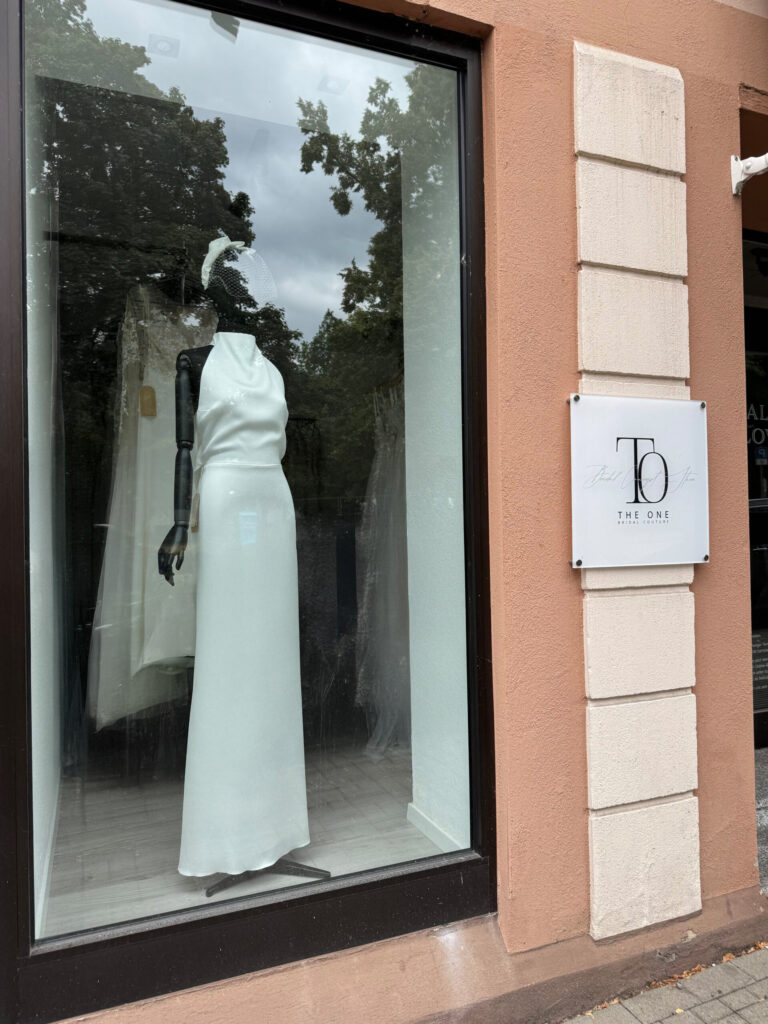 Ein weißes Hochzeitskleid wird auf einer Schaufensterpuppe in einem Schaufenster neben einem Schild mit der Aufschrift THE ONE ausgestellt.