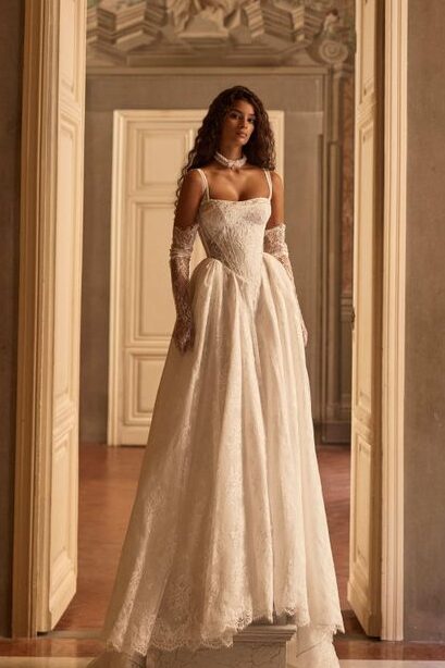 Eine Frau in einem eleganten weißen Kleid steht auf einem Sockel in einem prächtigen Saal mit kunstvoller Architektur und offenen Türen.